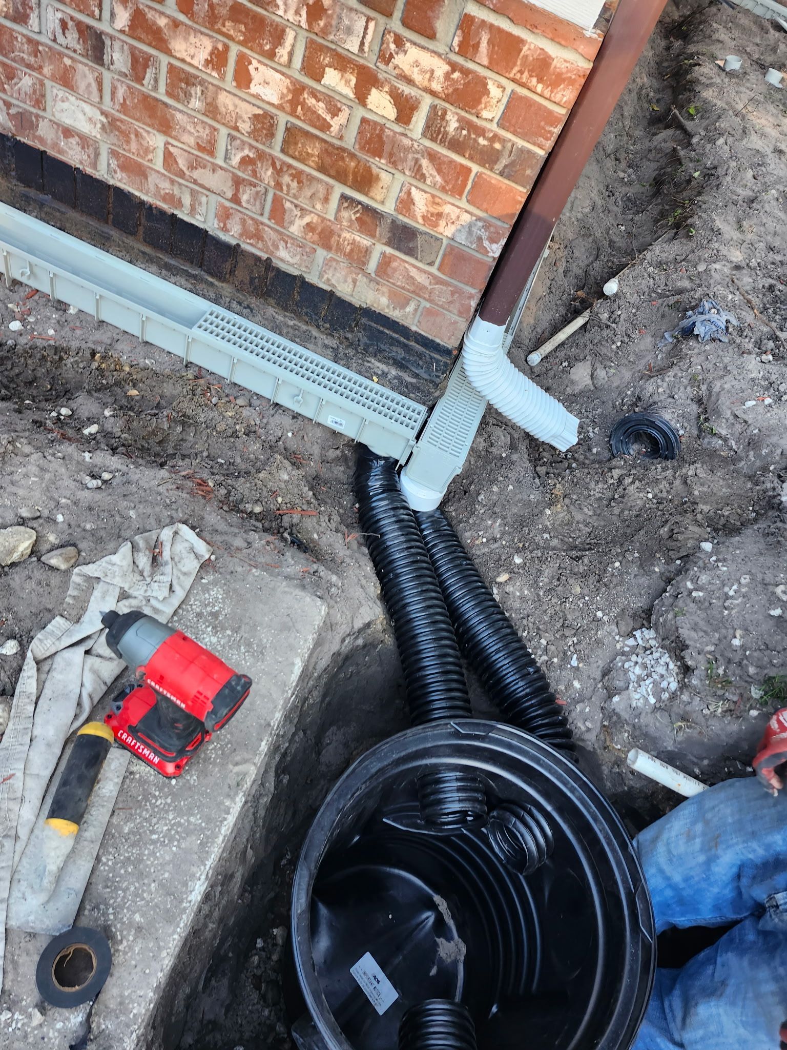 Construction of a drainage system: trench, corrugated pipe, catch basin, gutter, brick wall, and tools.