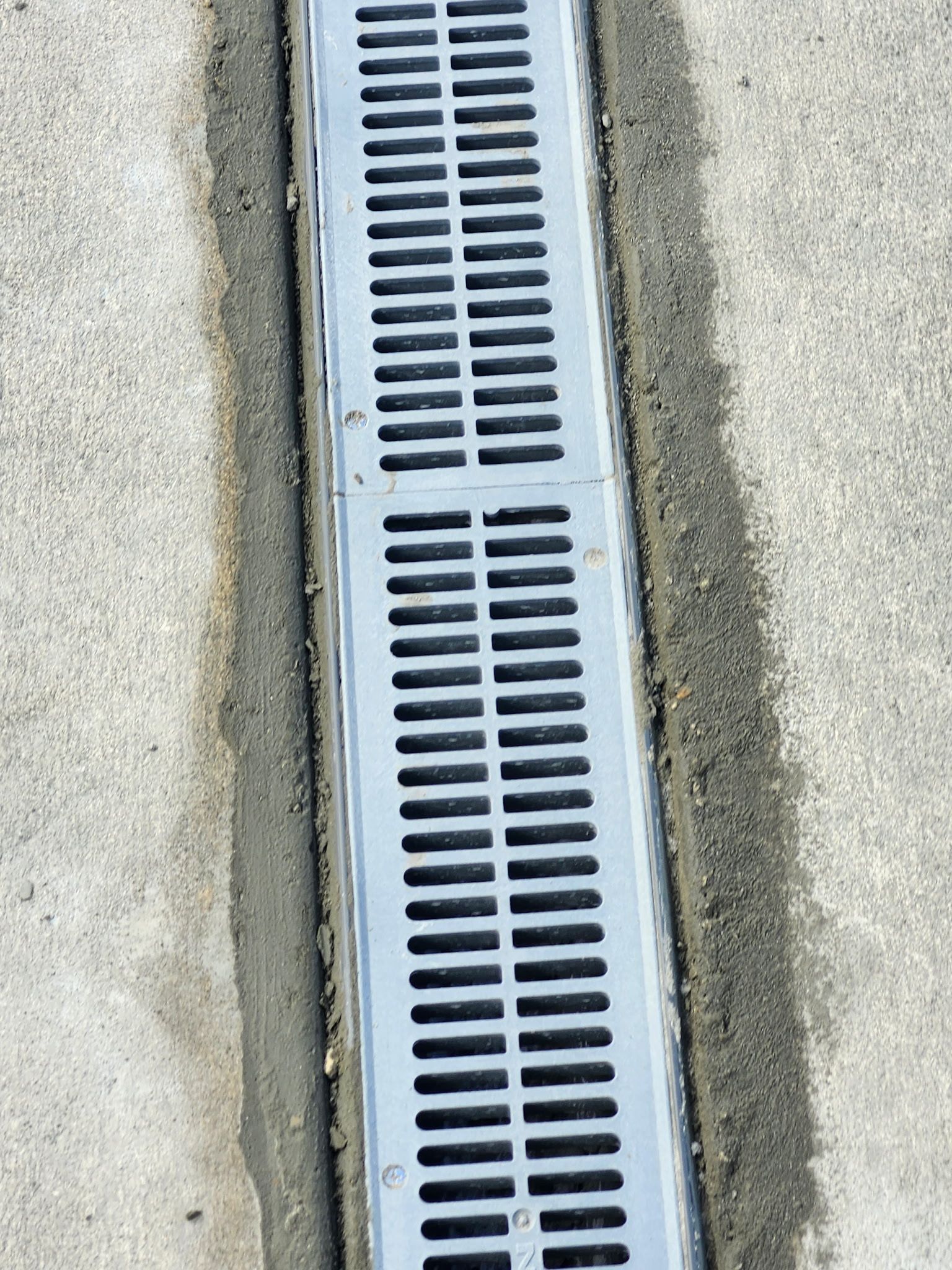 A gray linear drain with horizontal slots set in concrete.