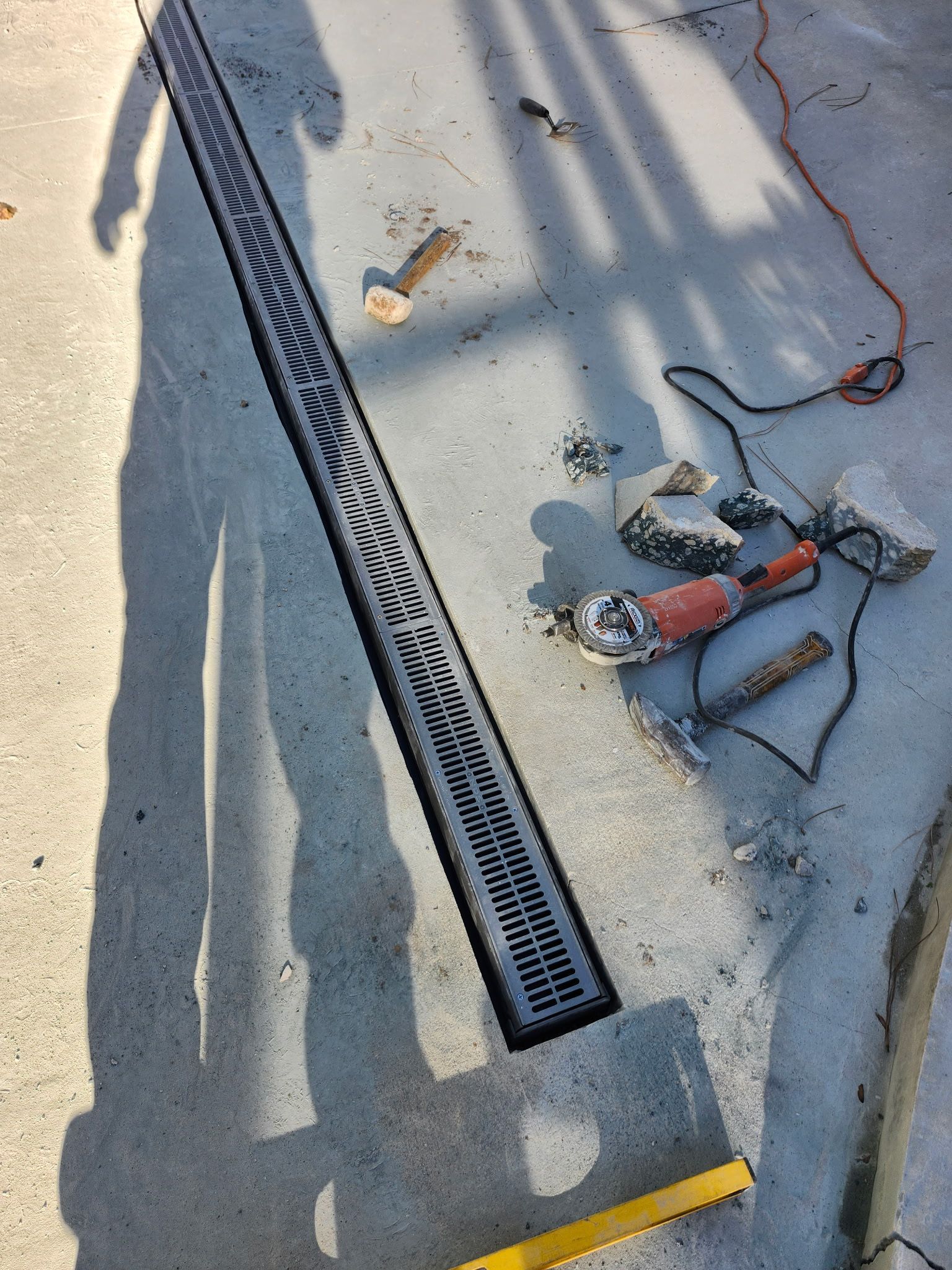 Concrete trench drain with metal grate being installed. Tools and debris surround it.
