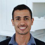 A man with a beard is smiling for the camera in a kitchen.