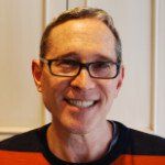 A man wearing glasses and a striped shirt is smiling for the camera.