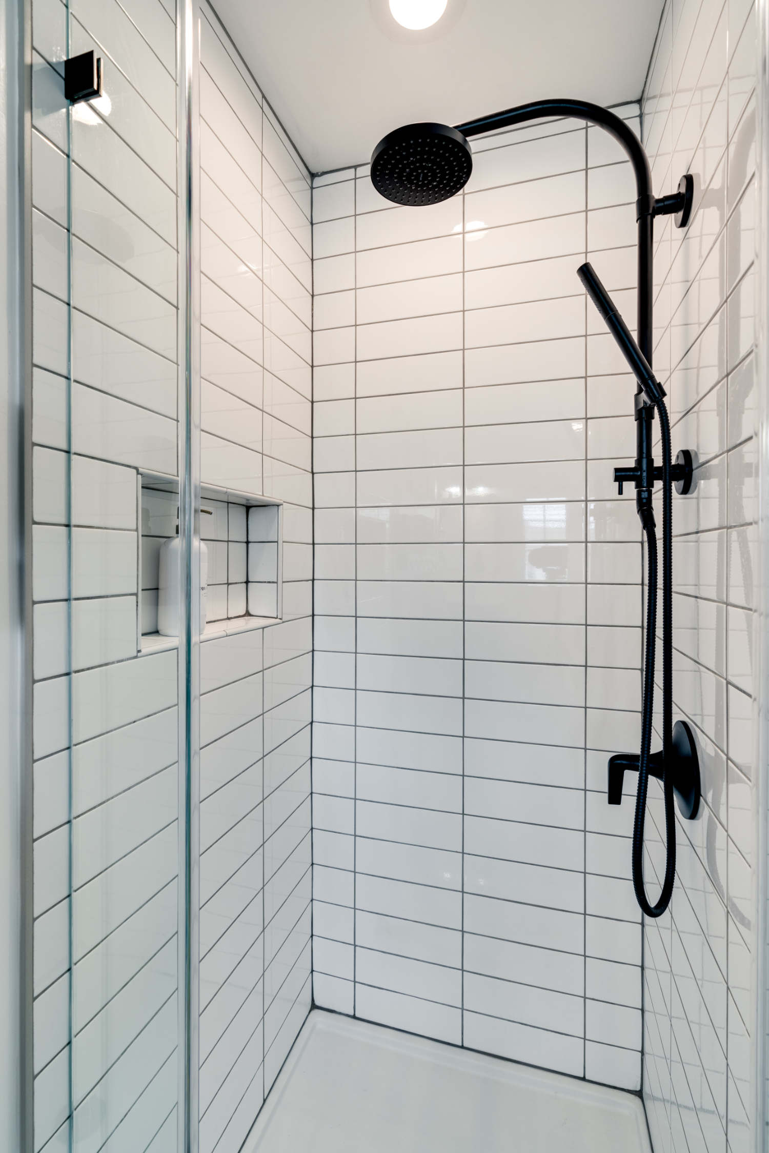 A shower with white tiles and a black shower head