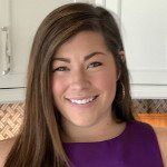 A woman in a purple shirt is smiling in a kitchen.
