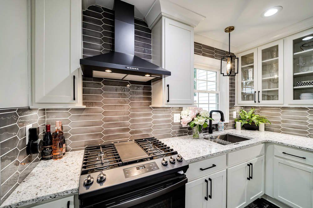A kitchen with white cabinets , a stove , a sink and a hood.