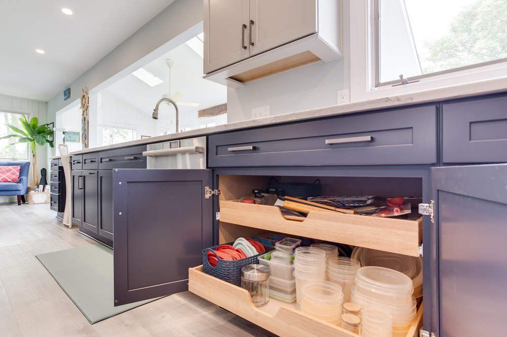 A kitchen with blue cabinets and a pull out drawer filled with utensils.