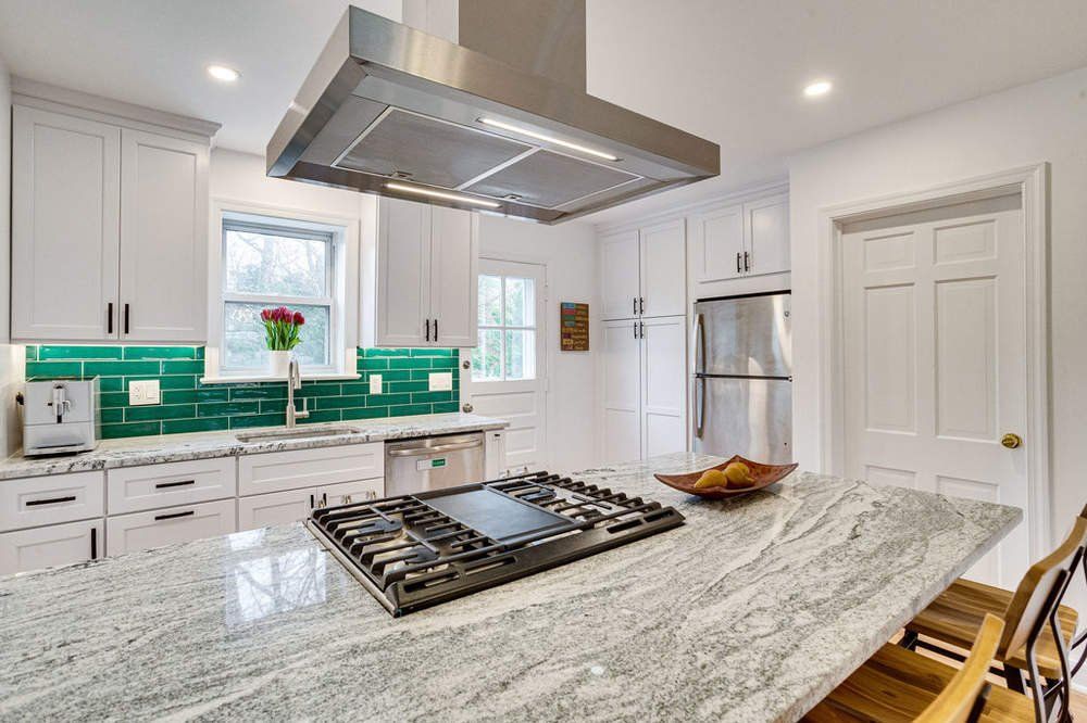 A kitchen with white cabinets , granite counter tops , stainless steel appliances and a stove top oven.