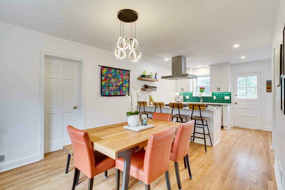 A dining room with a wooden table and chairs and a kitchen in the background.