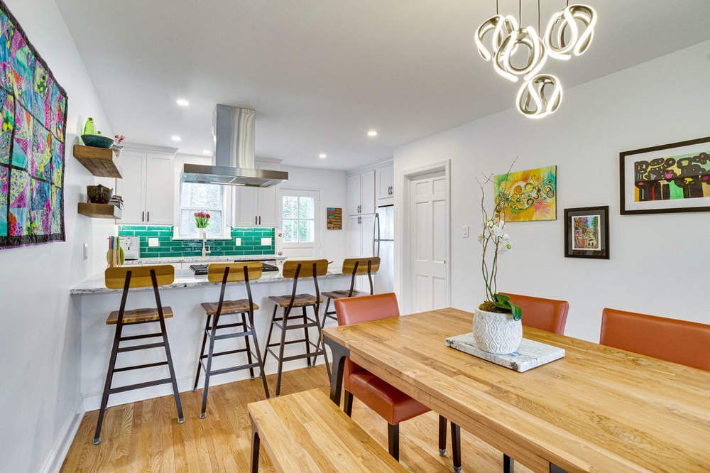 A dining room with a wooden table and chairs and a kitchen in the background.