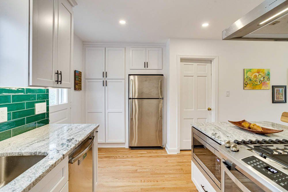A kitchen with stainless steel appliances , white cabinets , granite counter tops , and a refrigerator.
