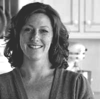 A black and white photo of a woman smiling in a kitchen.