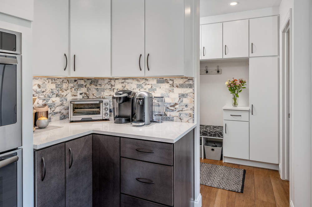 A kitchen with white cabinets , gray cabinets , a microwave , and a coffee maker.