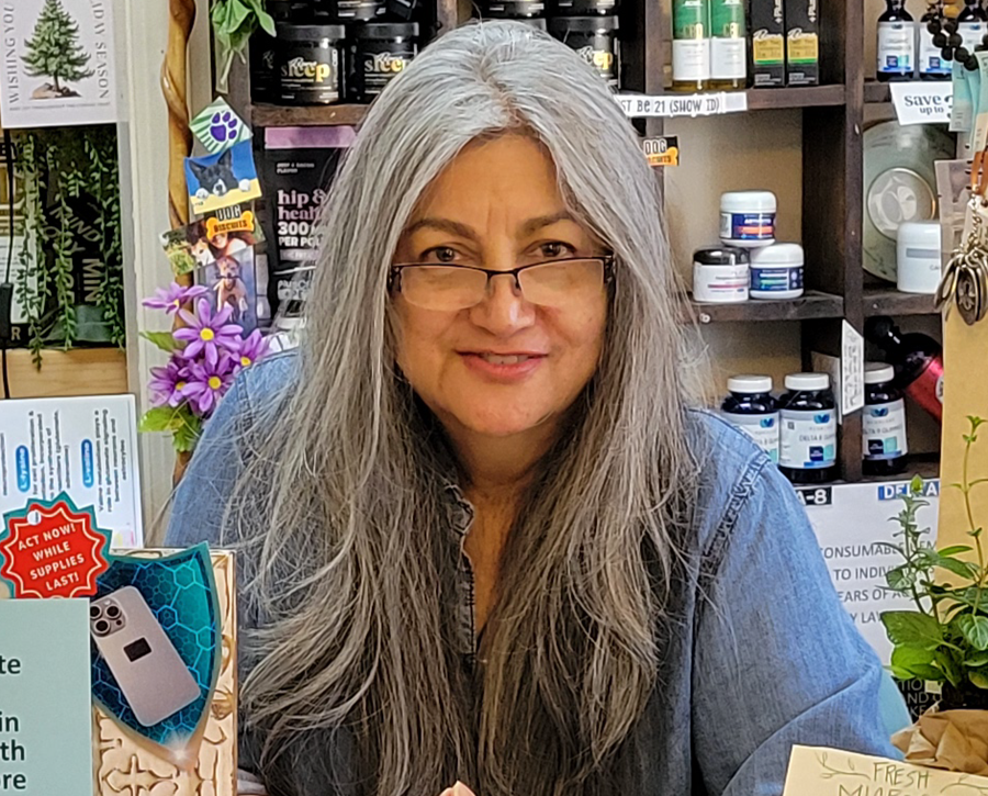 Woman with gray hair and glasses smiling in a shop, surrounded by shelves of products.
