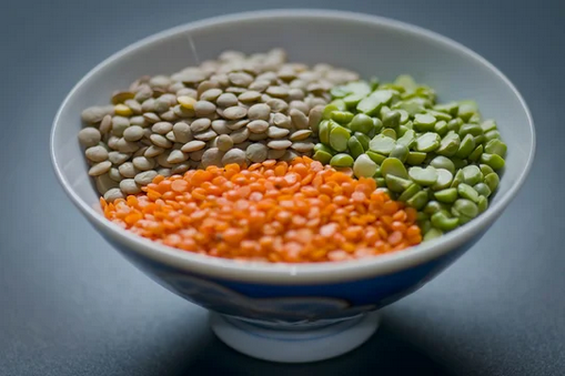 Bowl of lentils, split peas, and red lentils, segmented and on a dark surface.