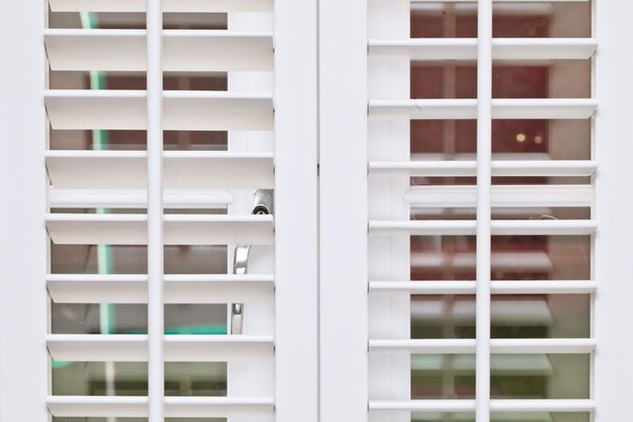 Close up of white shutters open over glass patio doors.