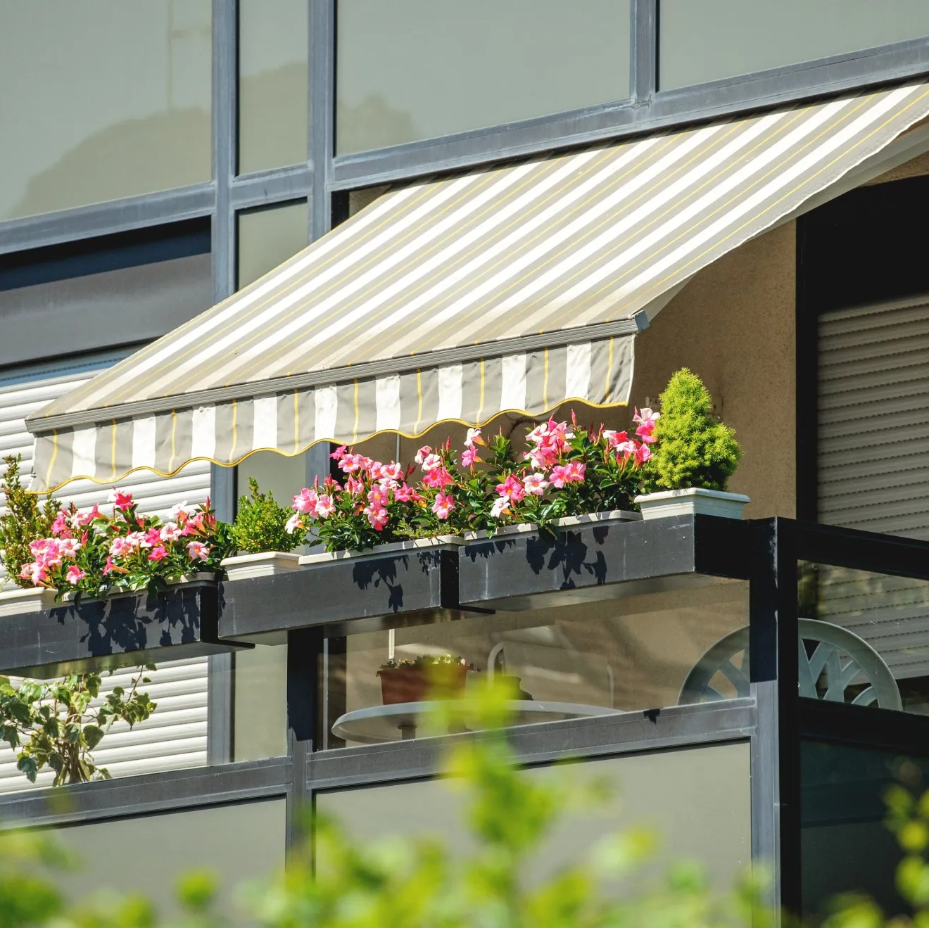 Outdoor striped awning covering first floor balcony with potted plants on railing.