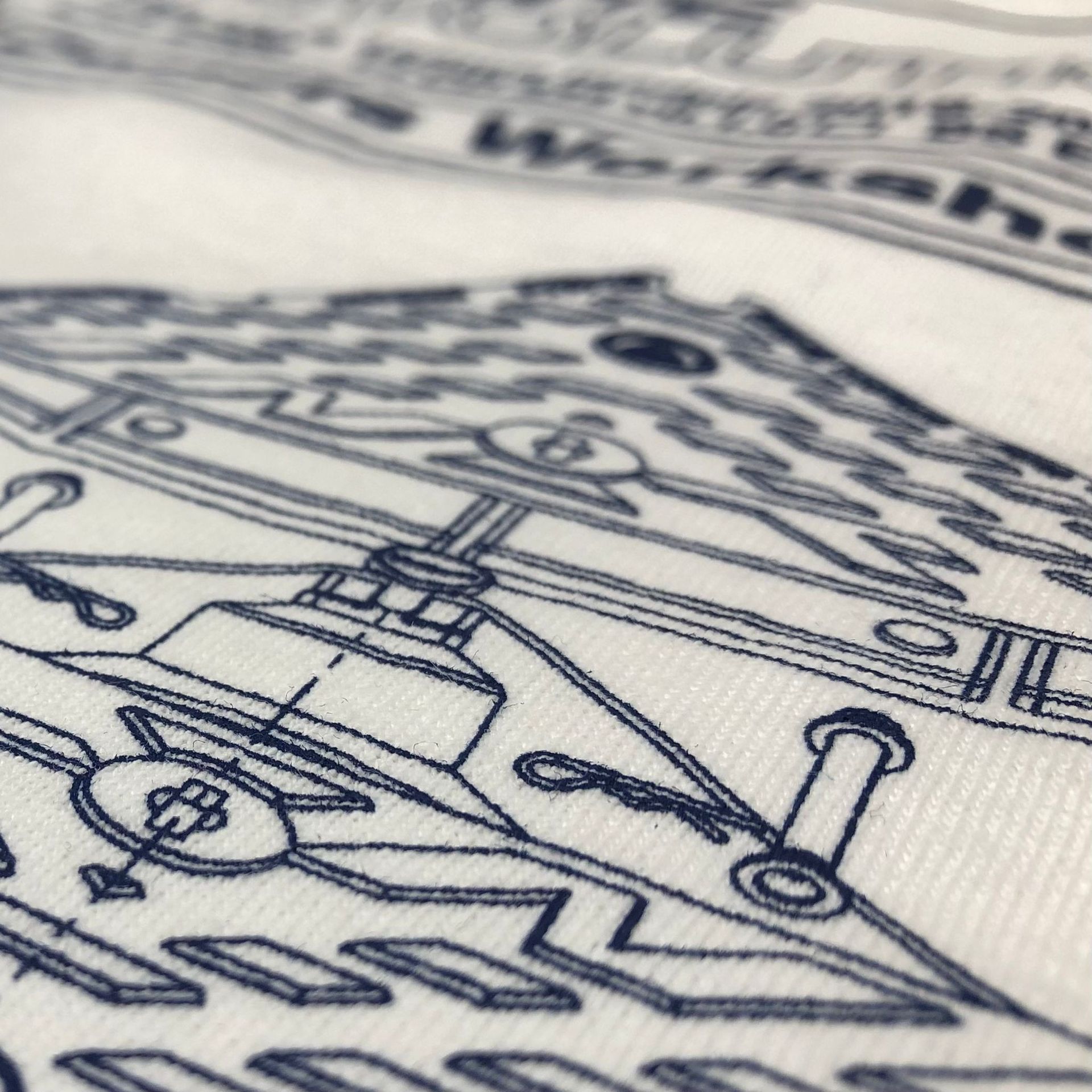 WhiteLodge Close-up of a white fabric with detailed dark blue schematic drawings of machinery, possibly a workshop.