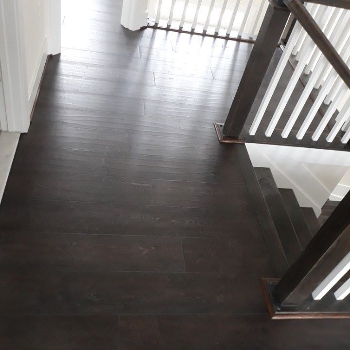 Dark wood flooring in a residential hallway, leading to a wooden staircase with white balusters.