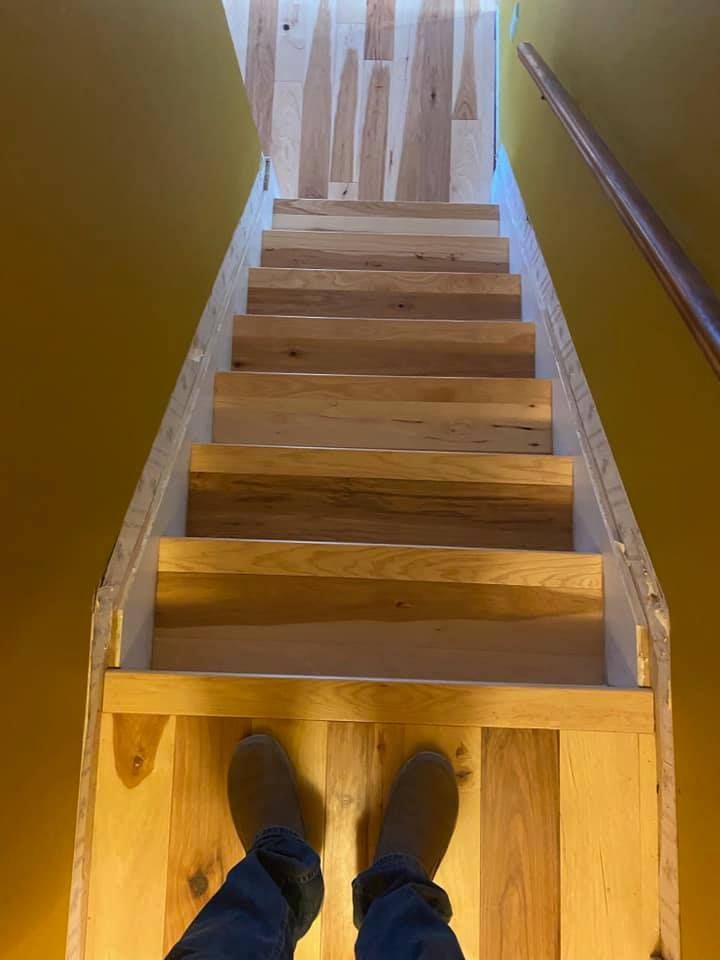 A first-person view looking down a narrow wooden staircase between yellow walls towards a landing.