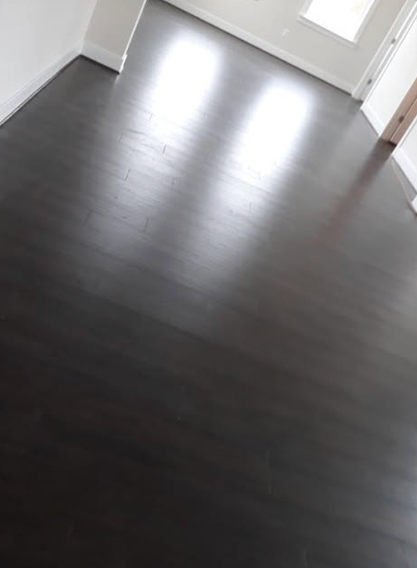 A high-angle view of a room with polished dark hardwood flooring, white baseboards, and bright natural light.