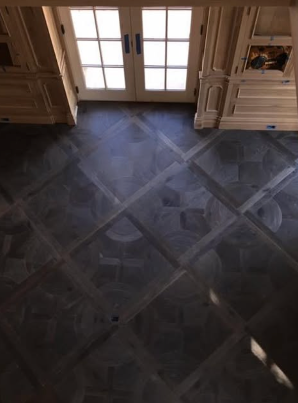 A high-angle view of a room with dark, patterned hardwood flooring, light wood cabinetry, and double glass doors.
