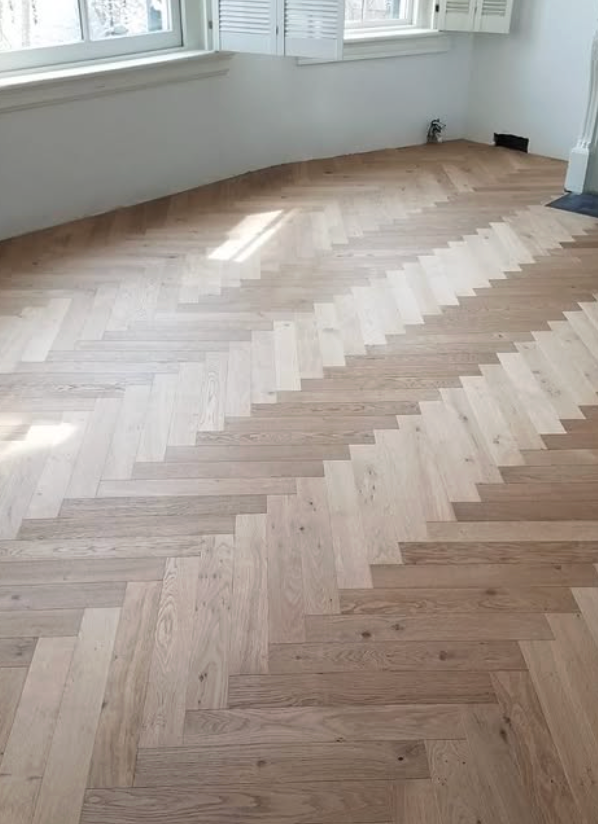 A light-toned wooden floor installed in a herringbone pattern with distinct diagonal bands of varied wood grain.