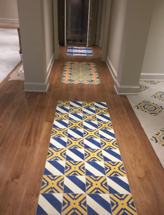 A hallway with hardwood floors featuring three repeating blue, yellow, and white geometric tile rug patterns.