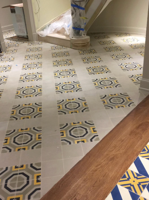 A person in blue gloves kneels, applying mortar to a tile floor with a trowel, laying tiles.