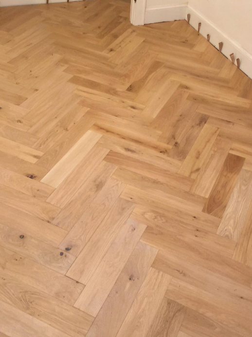 Light-colored oak wood flooring installed in a classic herringbone pattern with visible wood grain and knots.
