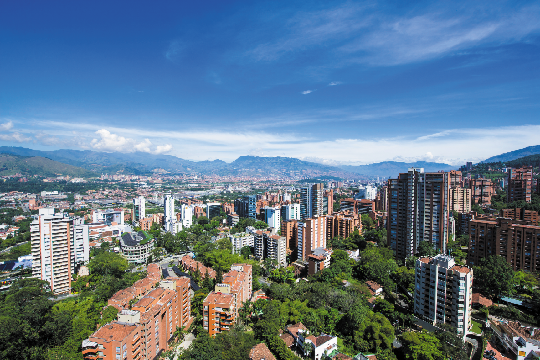 Panorámica de Medellín con montañas verdes, edificios modernos bajo un cielo despejado.