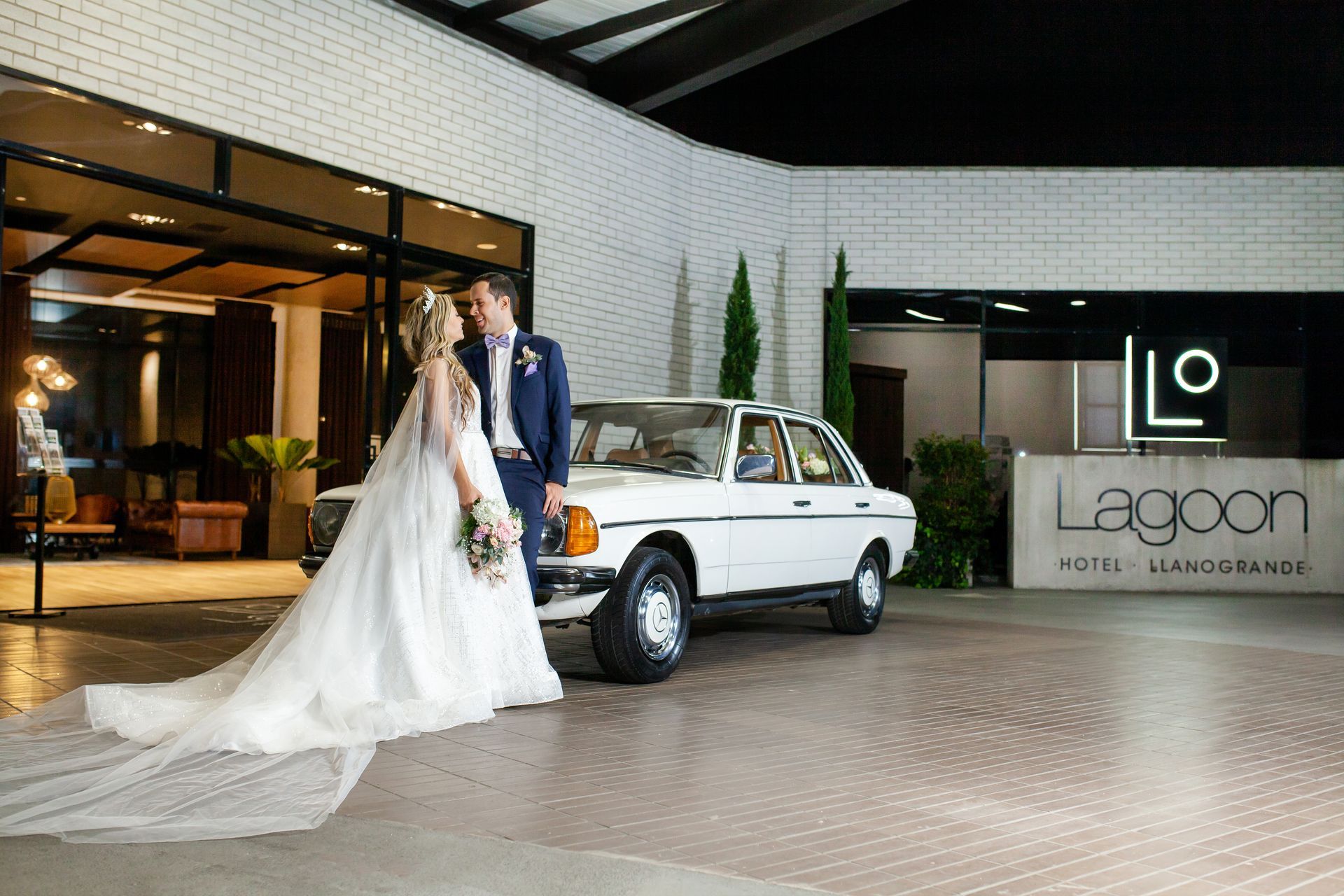 Una novia y un novio están de pie junto a un coche blanco  hotel Lagoon Llanogrande