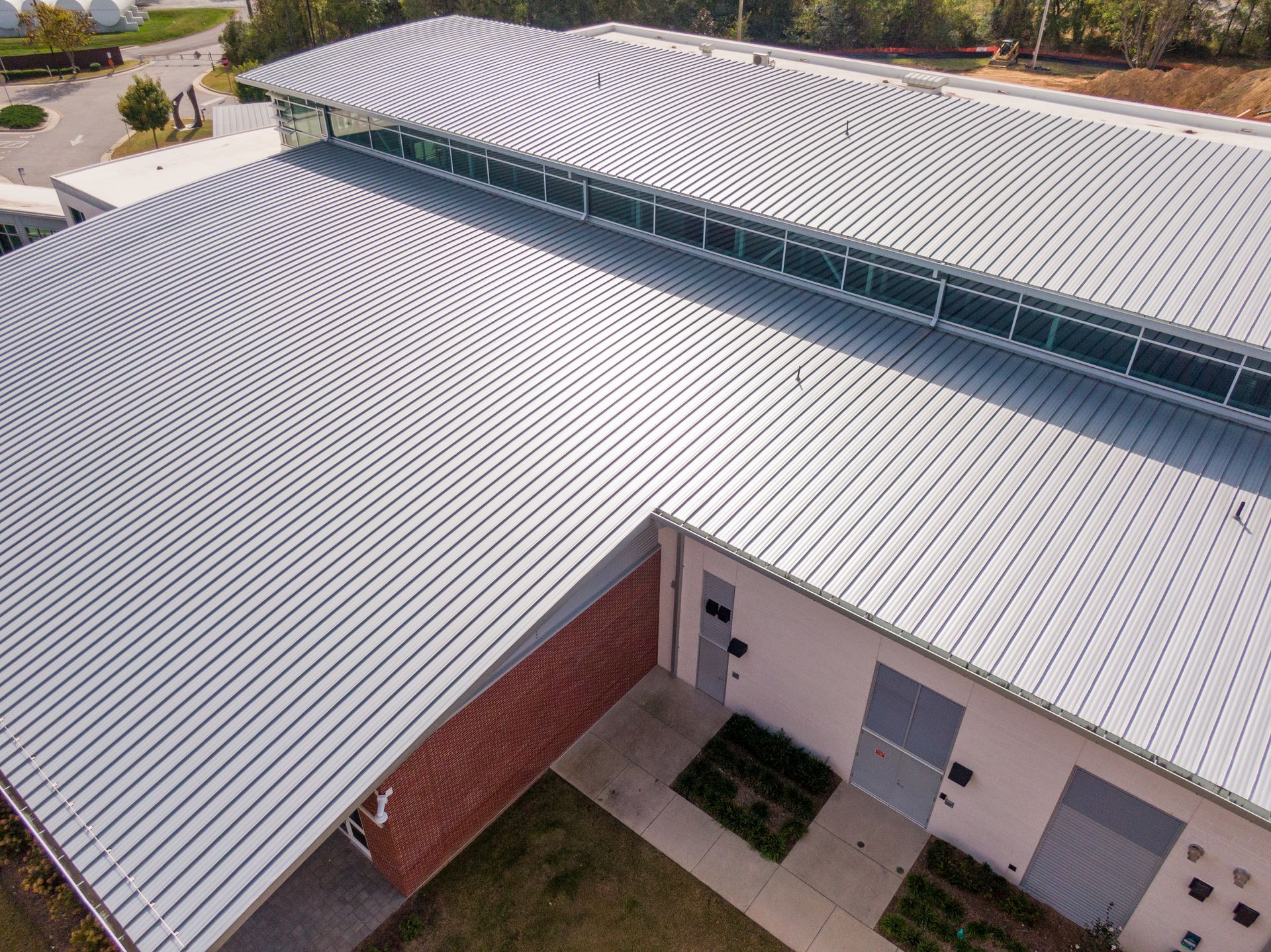Aerial view of a building with a corrugated metal roof. Red brick wall on the side, glass windows along the roofline.