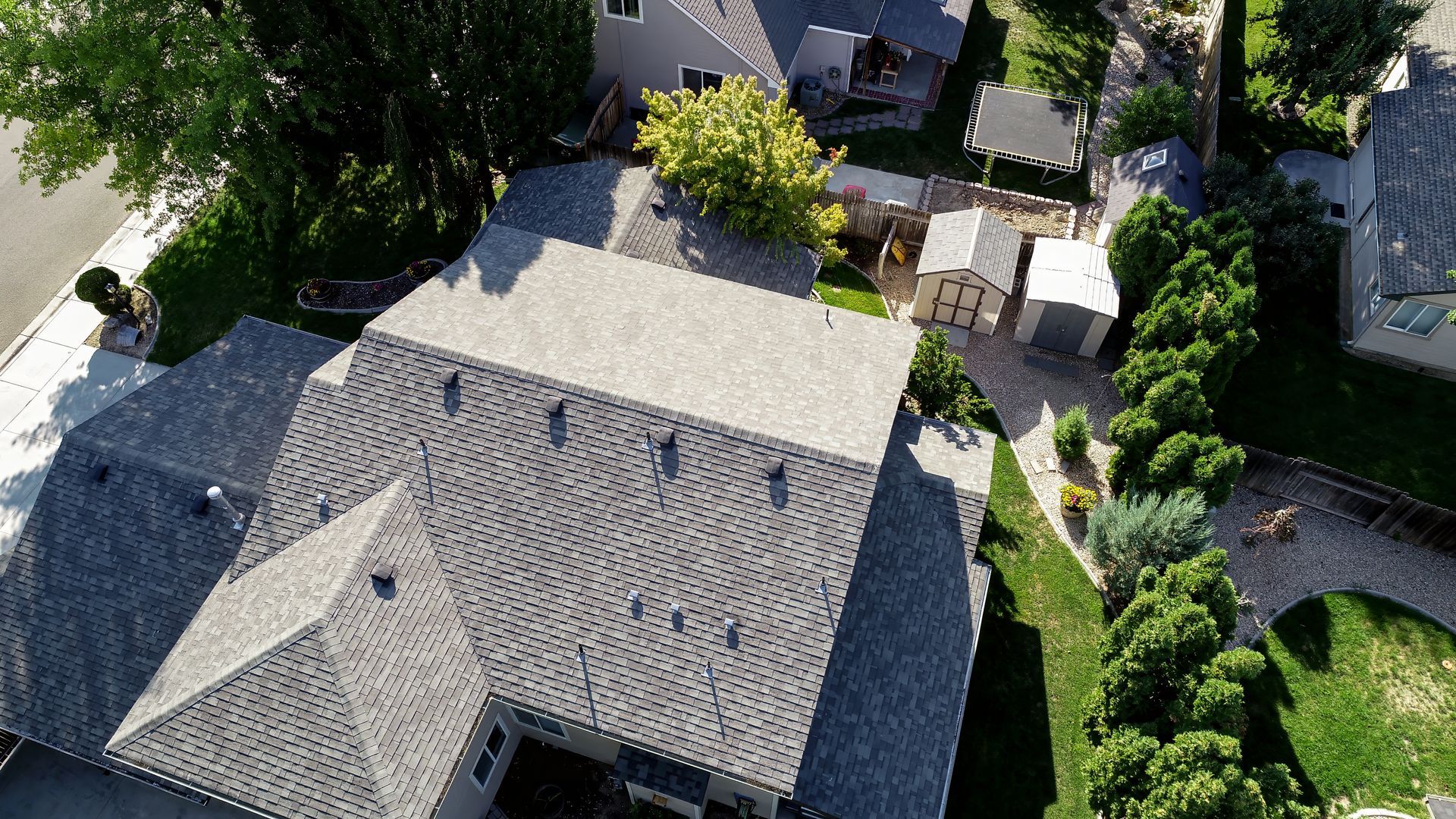 Aerial view of a gray roofed house with a yard, shed, and green trees.
