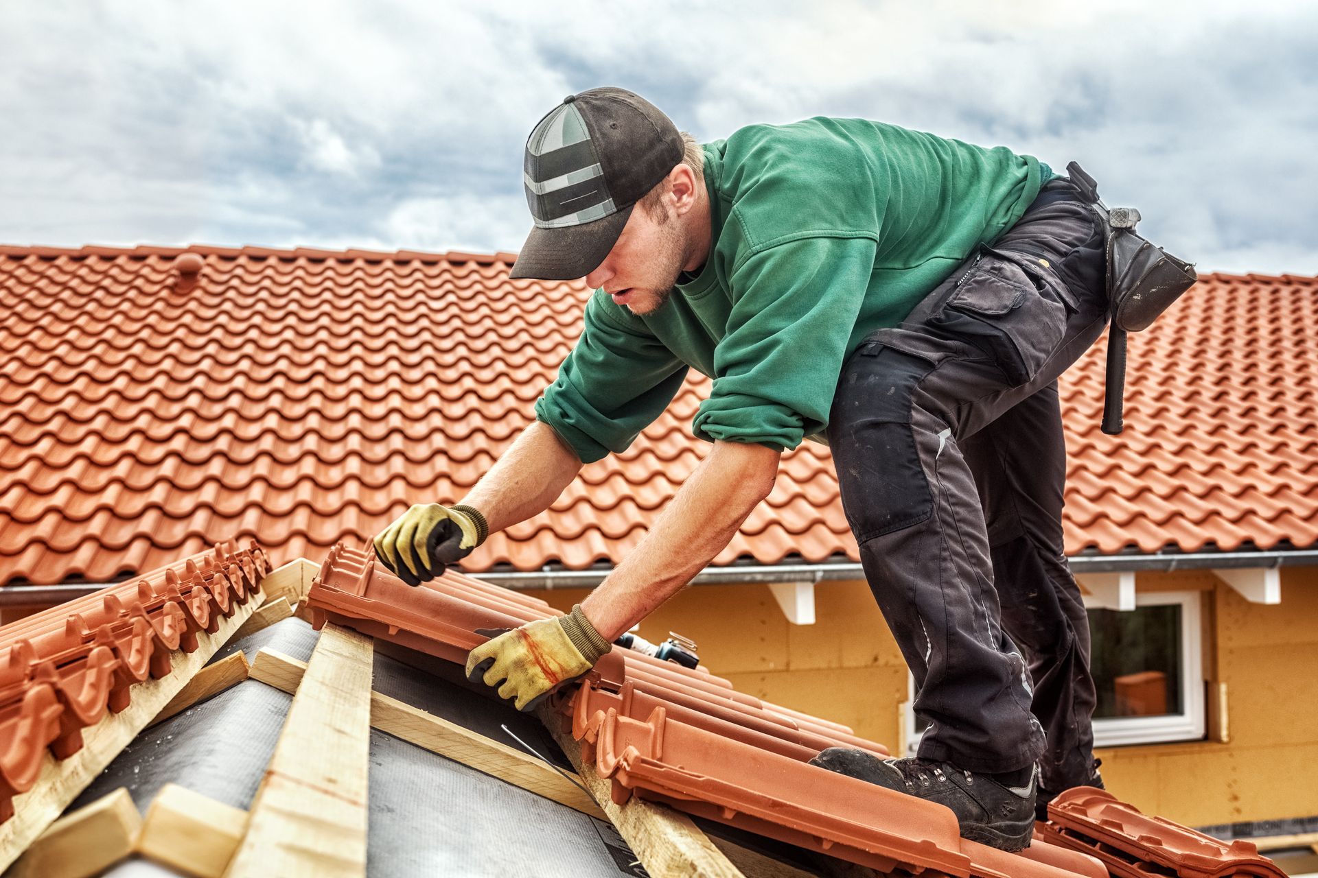 A roofer installing clay tiles on a sloped roof during a home construction project. A roofer installing clay tiles on a sloped roof during a home construction project.