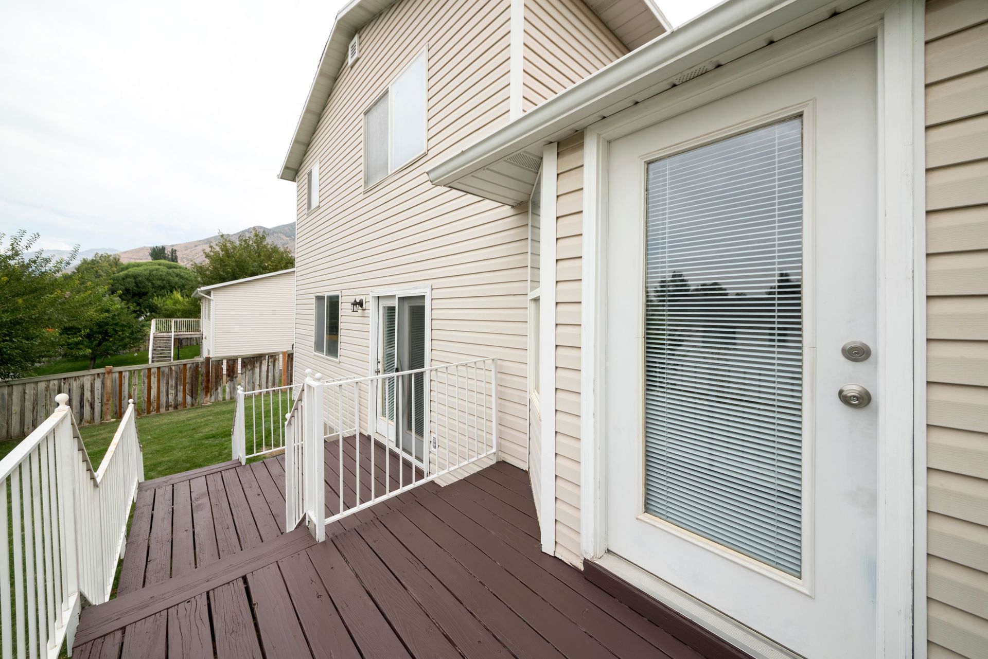Back deck with white railings, brown wood deck, and French door leading into a two-story beige house.