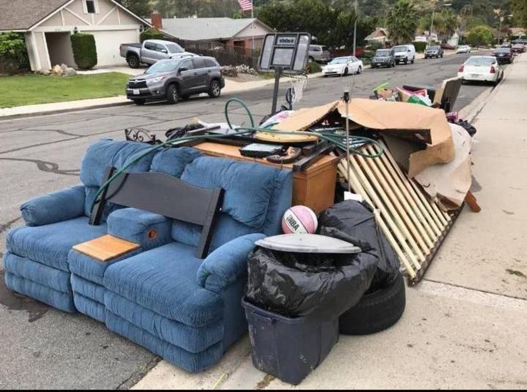 Couch, mattress, and trash piled on a residential street curb after bulk pickup.