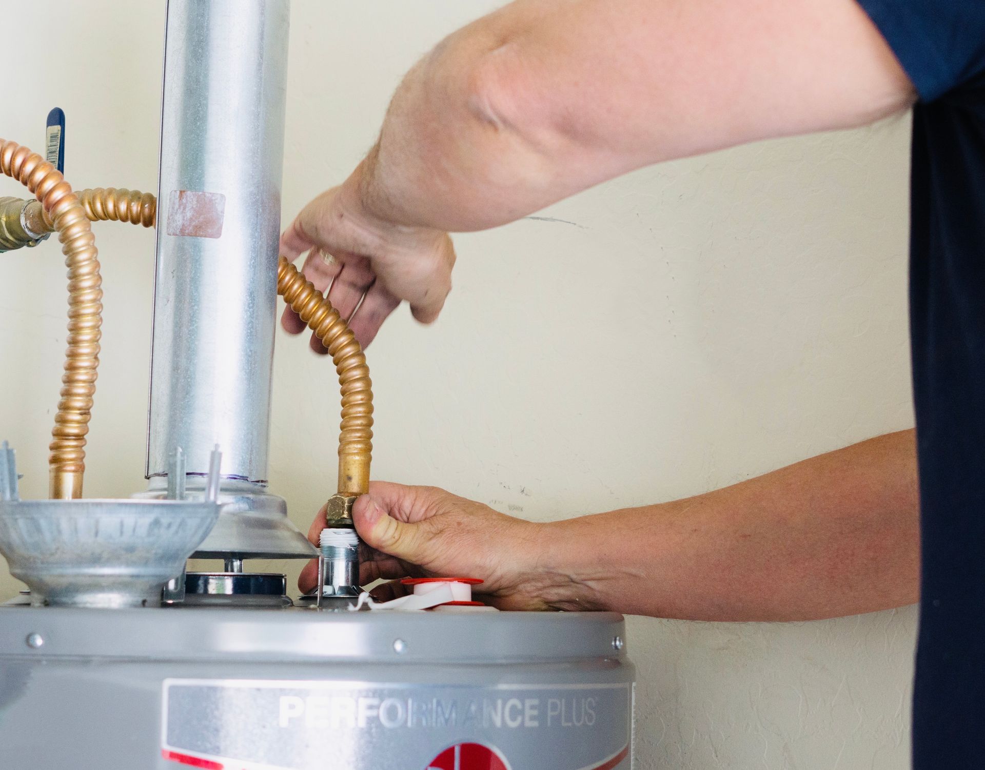 A person installing a flexible copper water line onto a water heater.