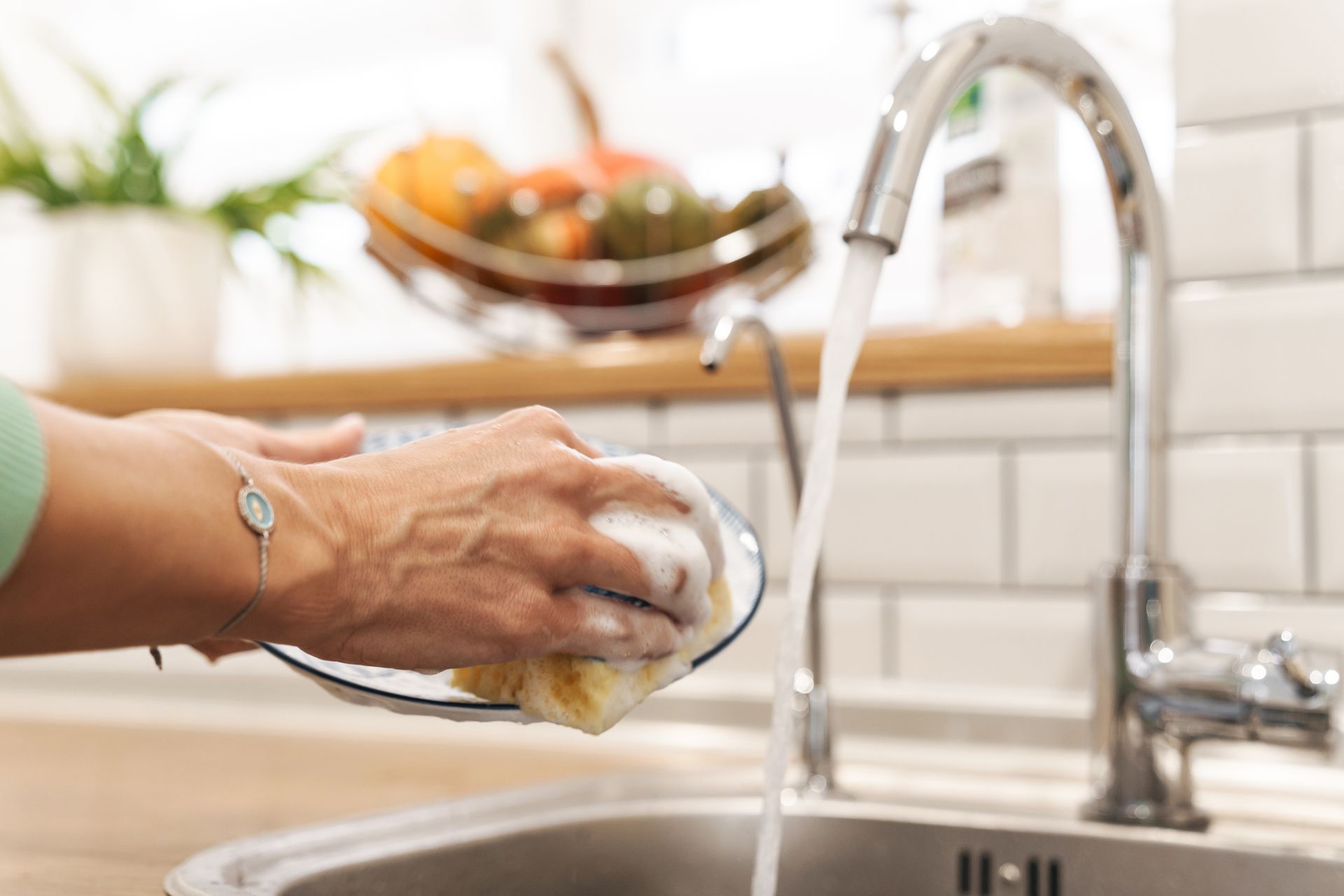Person washing a dish at a kitchen sink with running water, close-up.