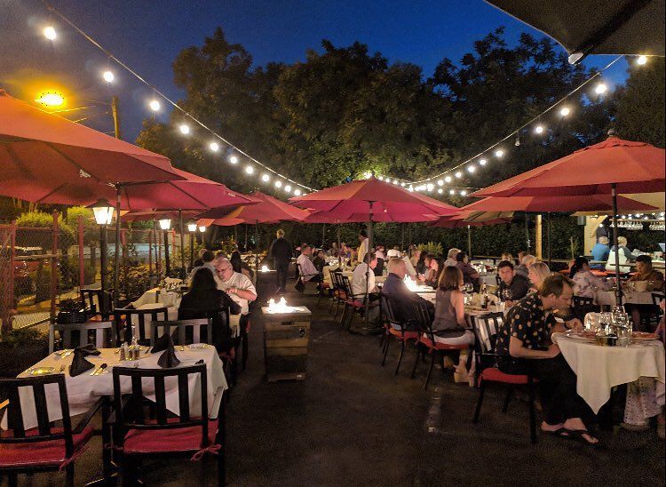 A group of people are sitting at tables under umbrellas at a restaurant.