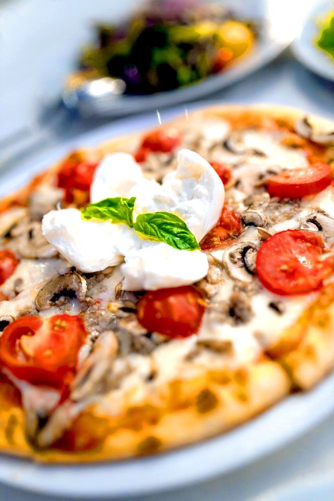 A pizza with mozzarella , tomatoes , mushrooms and basil on a white plate.