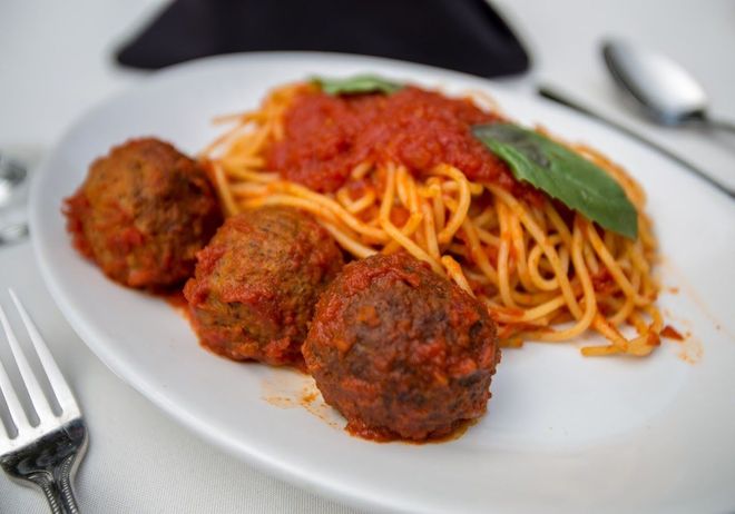 A plate of spaghetti and meatballs with sauce and basil on a table.