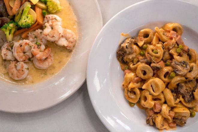 A plate of shrimp and a plate of pasta are on a table.