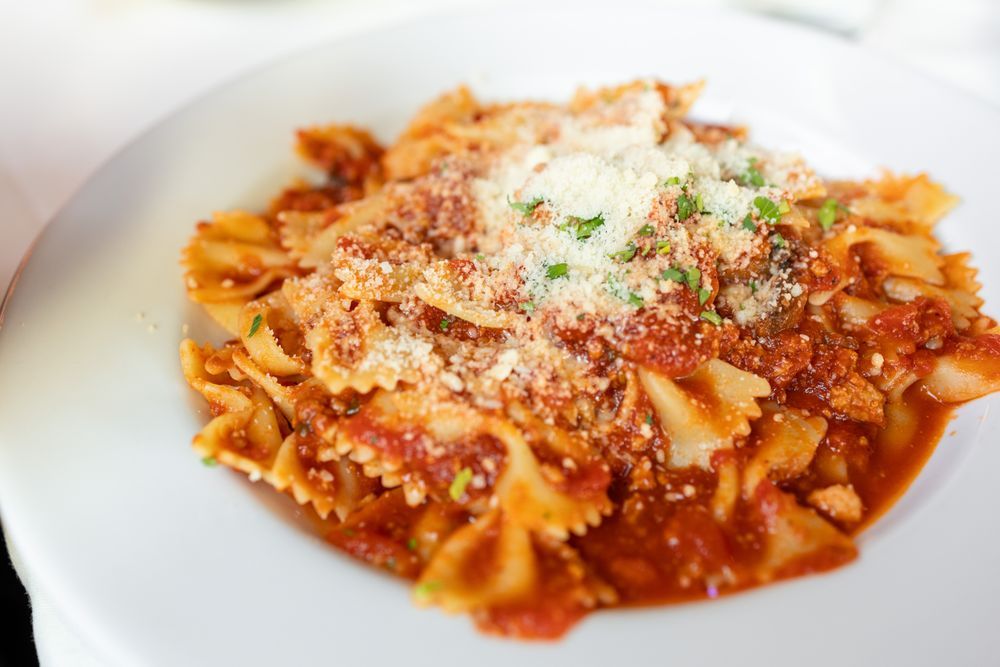 A close up of a plate of pasta with sauce and cheese on a table.