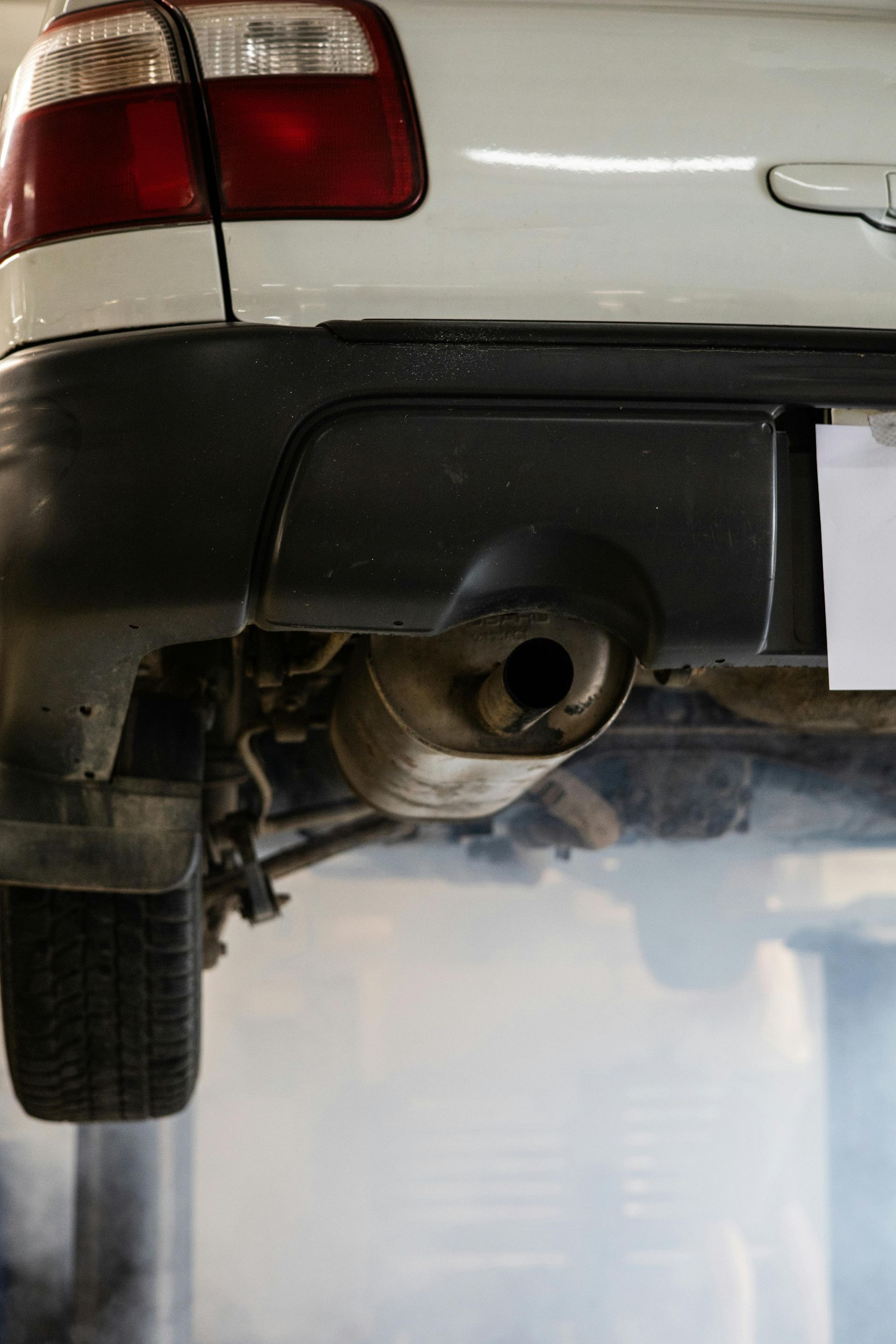 A white car is sitting on a lift in a garage with smoke coming out of the exhaust pipe.