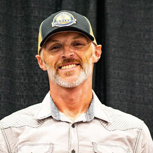 Man wearing a black baseball cap and t-shirt smiles at the camera.