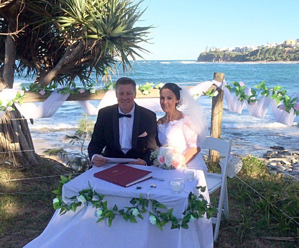 bridal couple sit at registry table ready to sign papers with ocean in the background