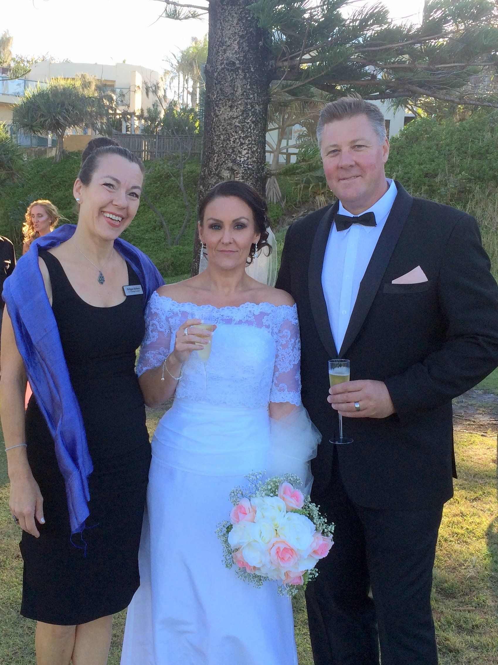 bride and groom posing with their Noosa celebrant, smiling and champagne for the couple