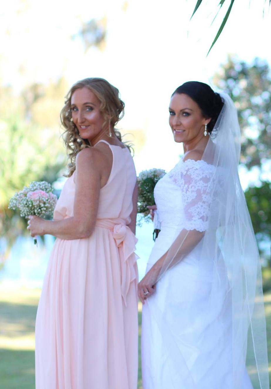 bride in white with her sister bridesmaid in pink with pink posy looking back