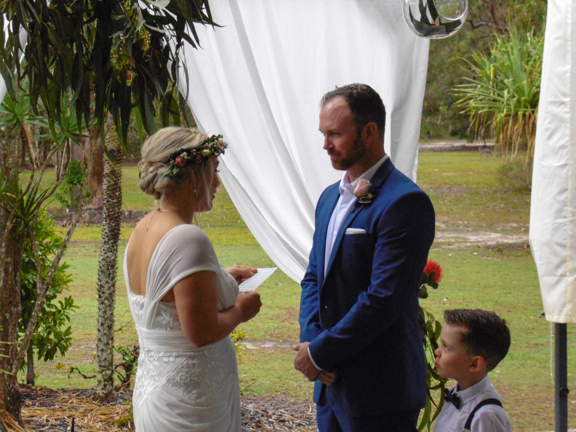 bride with flower crown reading her vows to husband in blue suit at their Noosa North shore wedding with children watching