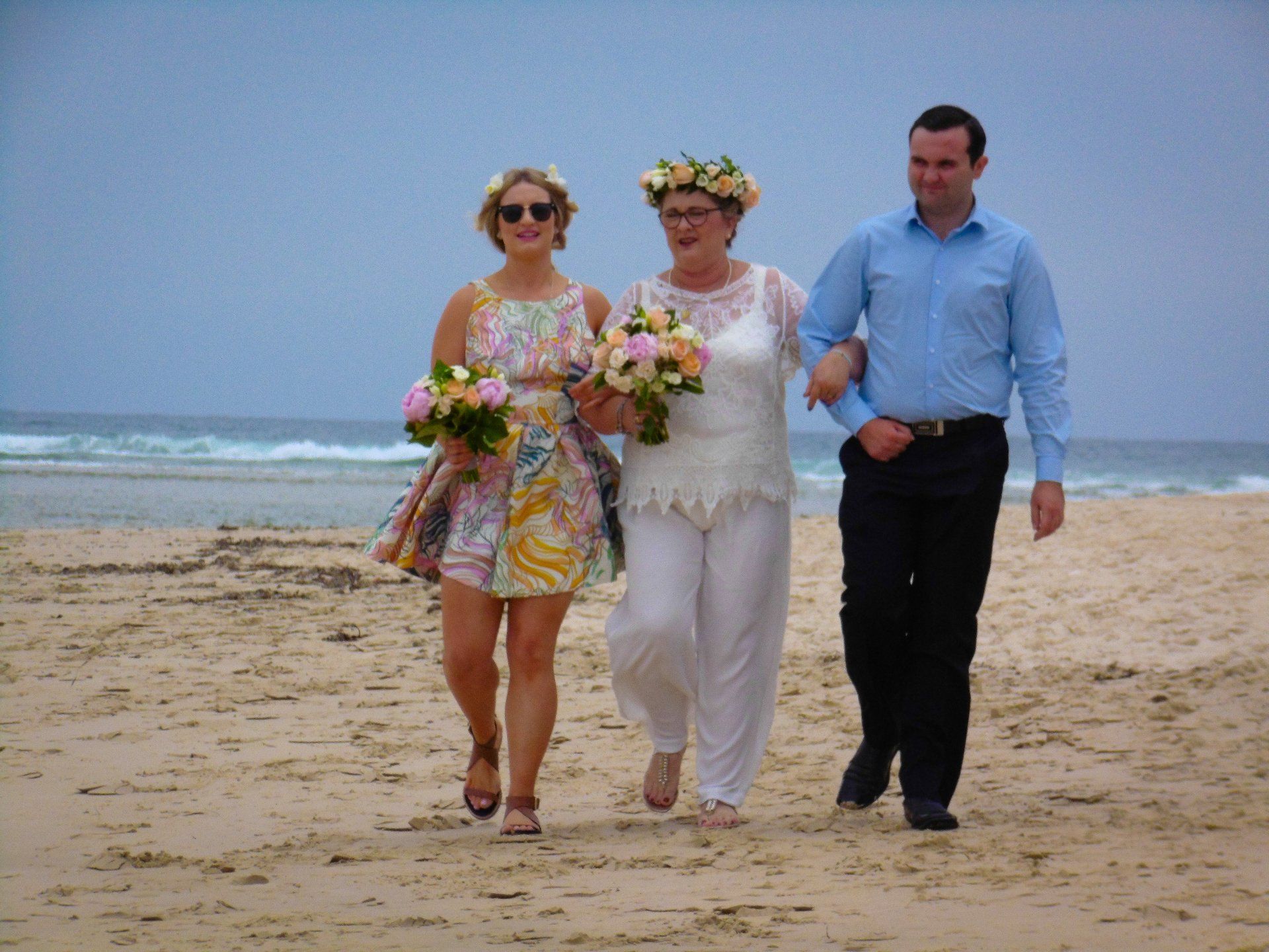 son and daughter walking their bride mother along sandy beach to get married at Noosa Spit with lots of flowers