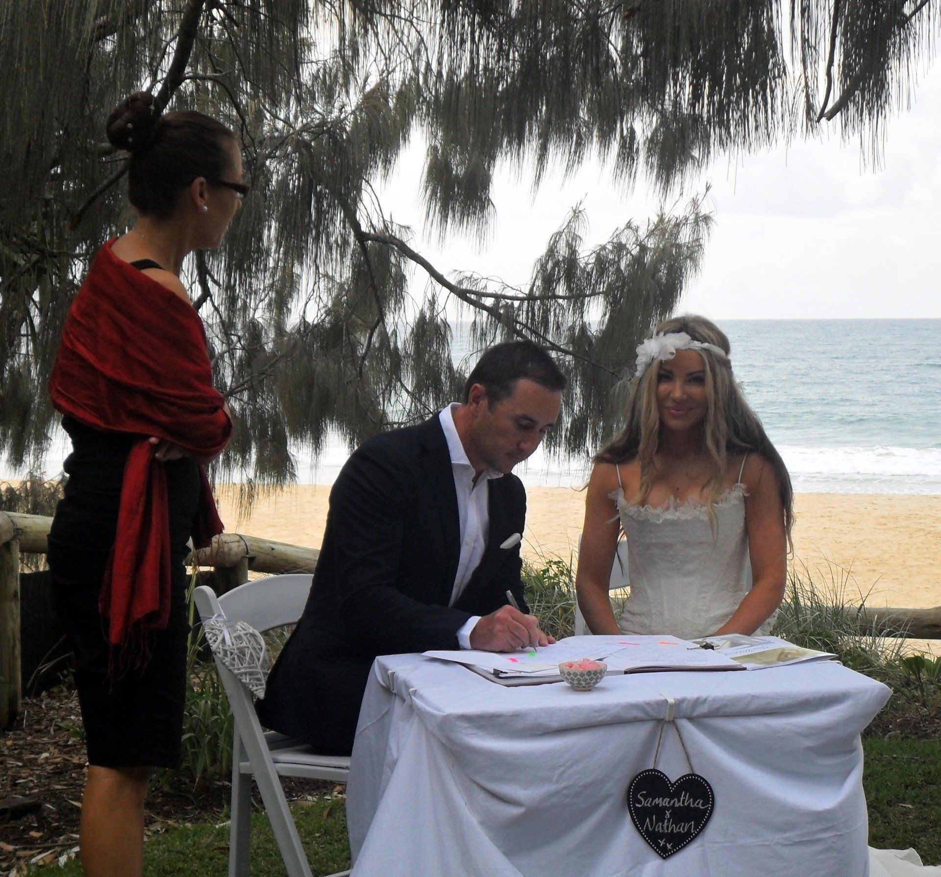 bride and groom sign papers at Noosa casuarina Grove at sunset, bride in white with tiara and groom in black suit